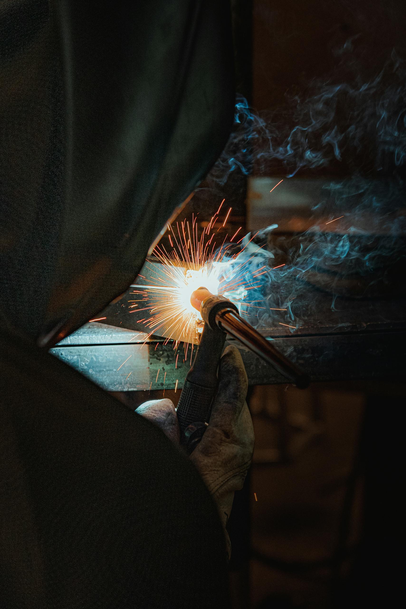 Close-up of a welder in action, creating sparks and smoke during metalwork, showcasing craftsmanship.